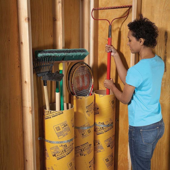 woman places a garden rake into a cardboard concrete tube in the garage