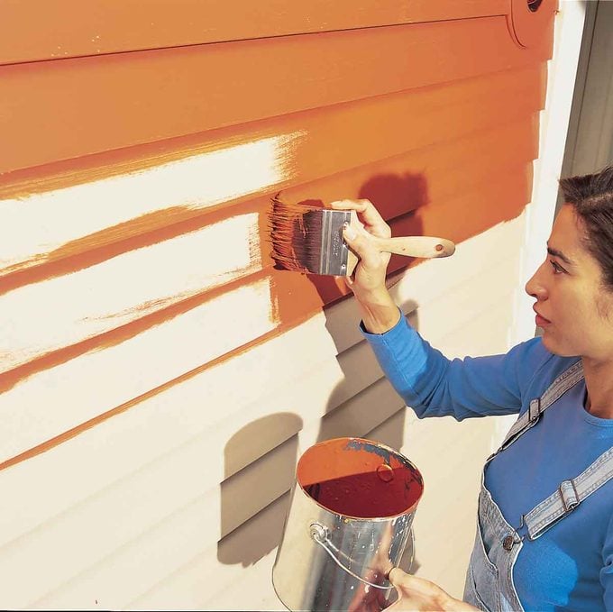 woman adds a coat of red-orange paint to a house