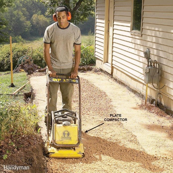 man operates a plate compactor along gravel in a backyard
