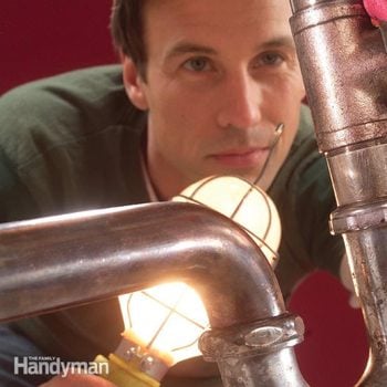 man shines light on under sink pipes