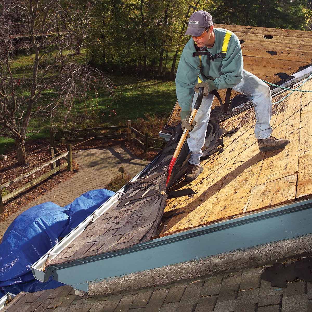 Roofing contractor prying up old roof shingles.