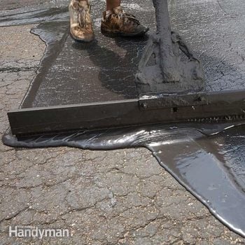 a squeegee pushes seal coat over a worn driveway