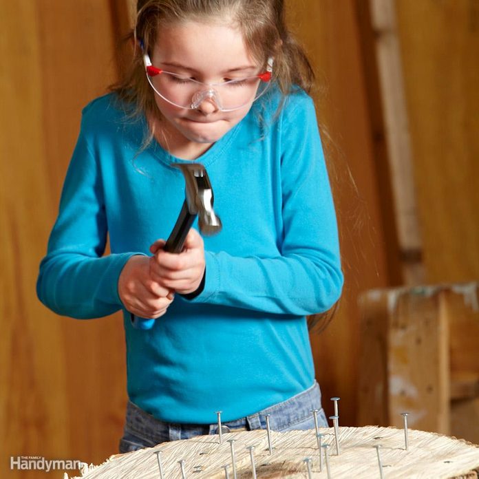 young girl uses hammer on nails in log