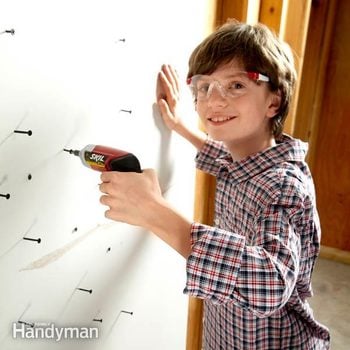 young boy smiles as he uses a drill on screws