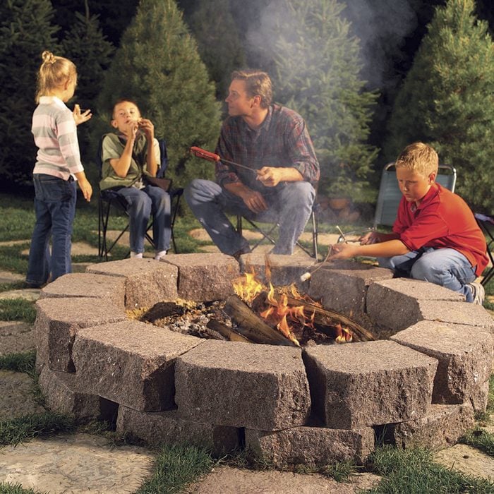 DIY fire pit fire ring backyard ideas Family roasting marshmellows around DIY firepit