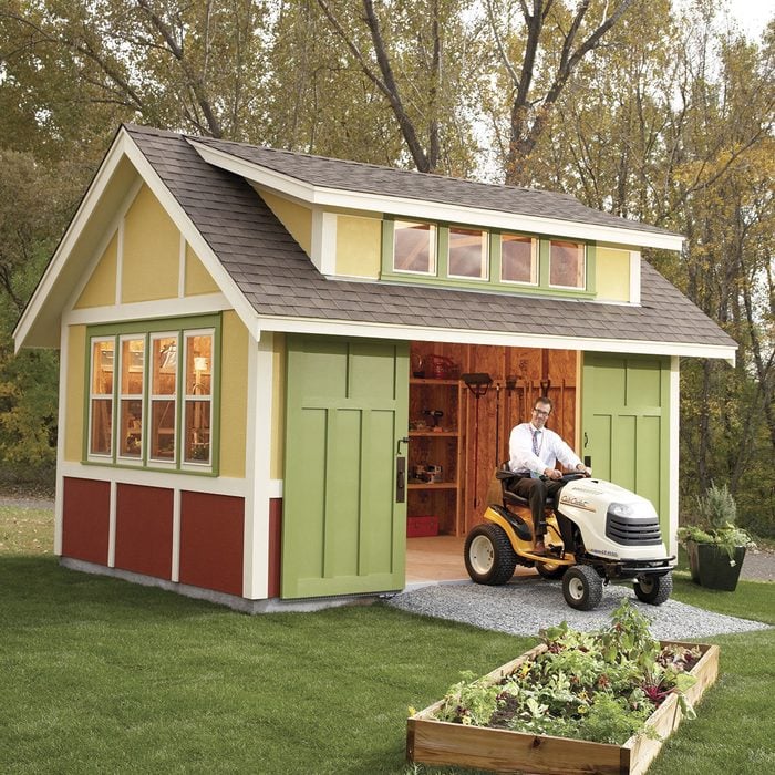 DIY garden shed backyard idea man driving tractor out of garden shed