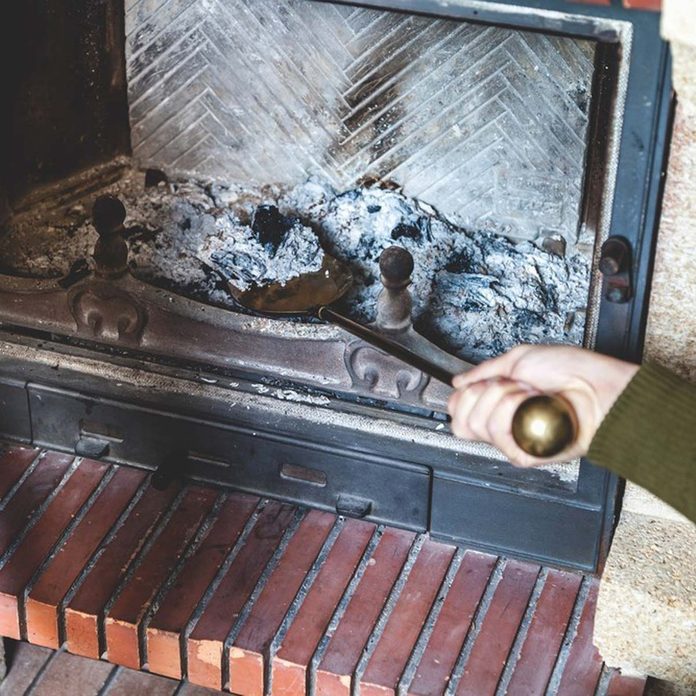 Cleaning the fireplace. Hand of man holding a brass shovel with ash