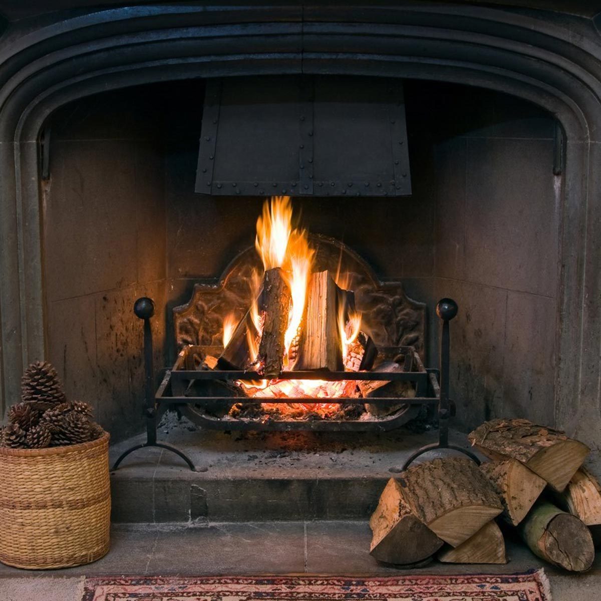 fire within a large stone arched fireplace, with pile of logs and basket of pine kernels