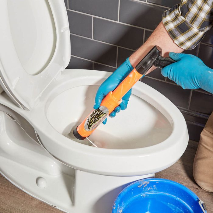 anonymous person draining water from a toilet using a squirt gun