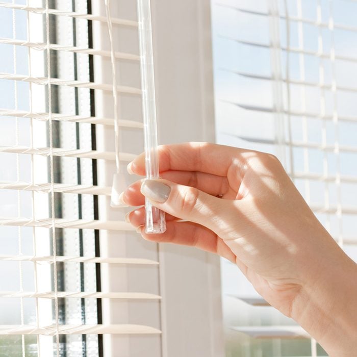 hand adjusting the blinds on a window