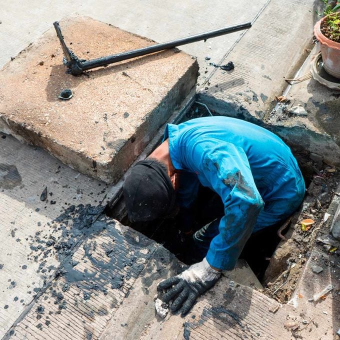 Plumber in a blue shirt is working on a sewer