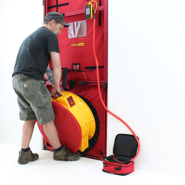Putting a fan in place for a blower door test | Construction Pro Tips