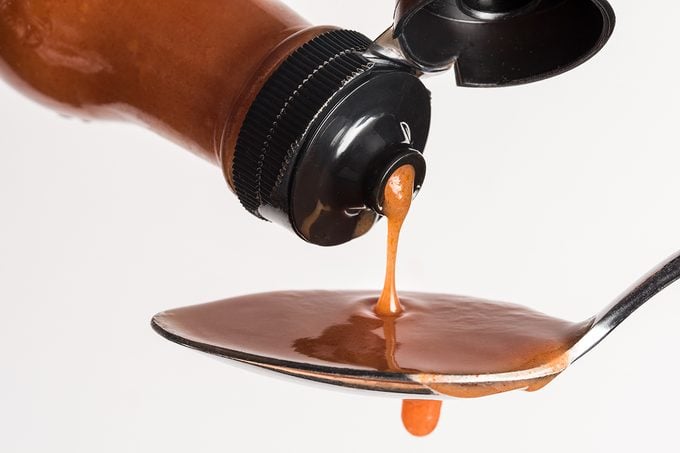 Close Up Of Bottle Pouring Hot Sauce In Spoon Against White Background