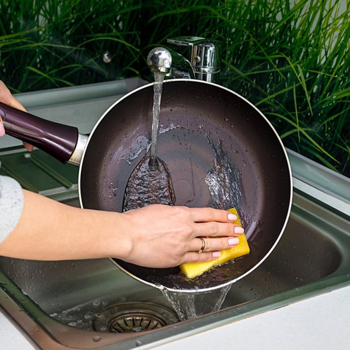 Female hand washing frying pan close up under running water, Young housewife woman washing griddle in a kitchen sink with a yellow sponge, Hand cleaning, manually, by hand, housework dishwasher,; Shutterstock ID 1079775416; Job (TFH, TOH, RD, BNB, CWM, CM): TOH