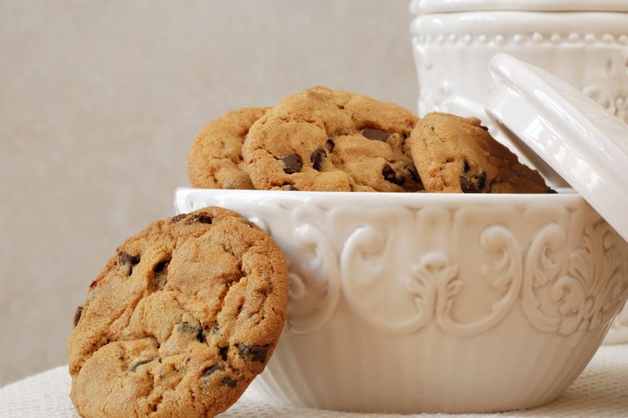 Freshly baked, chocolate chip cookies in a vintage dish with matching cookie jar in the background. Close-up with shallow dof.