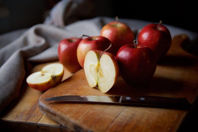 Bright juicy red apples lie on a vintage rustic table. Cut half of the Apple in the foreground.