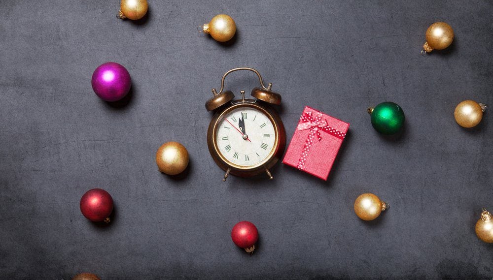 Gift and alarm clock with baubles on grey background