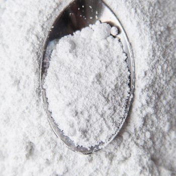 White powder in silver spoon over white background. Top view. Detailed close-up shot. Icing, caster, confectioners or powder sugar pile.