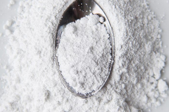 White powder in silver spoon over white background. Top view. Detailed close-up shot. Icing, caster, confectioners or powdere sugar pile.