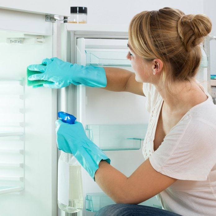 Young woman cleaning refrigerator with sponge and spray at home; Shutterstock ID 338967302