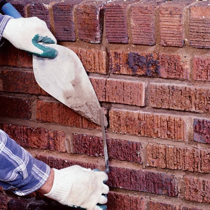 Woman adds motar mix to crack in bricks