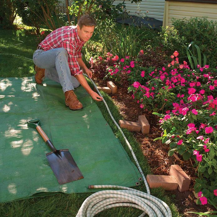 Man measures garden bed edge with a garden hose