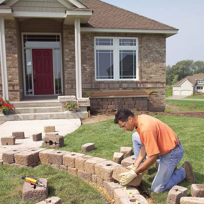 kneeling man adds landscaping stone to front yard