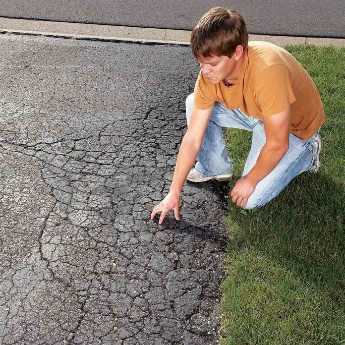 Man-examines-a-cracked-and-crumbling-asphalt-driveway