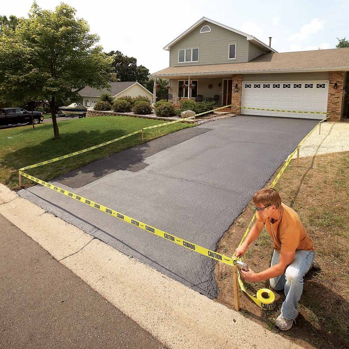 Man-kneels-to-staple-caution-tape-to-post-after-repaving-driveway