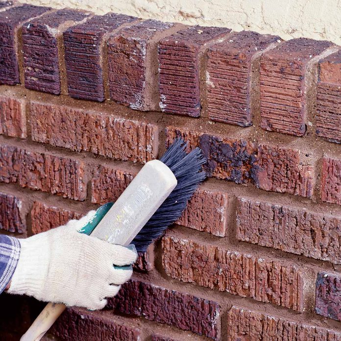 Woman brushes bricks clean after adding motar to joints