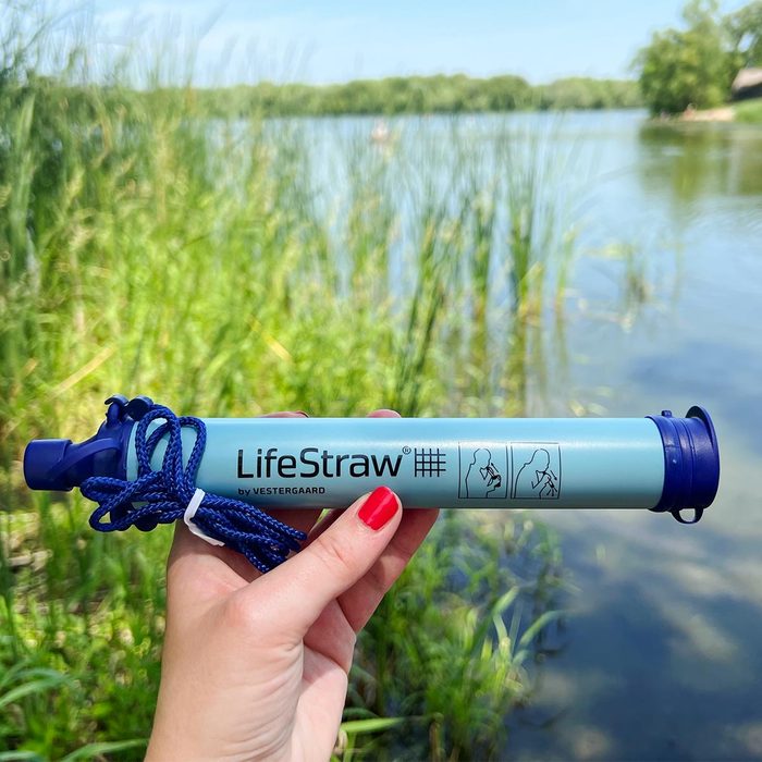 Lifestraw being held up in front of a pond in the background