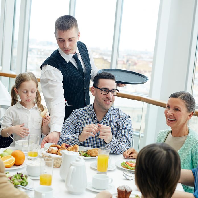 Young waiter serving big family during dinner or breakfast