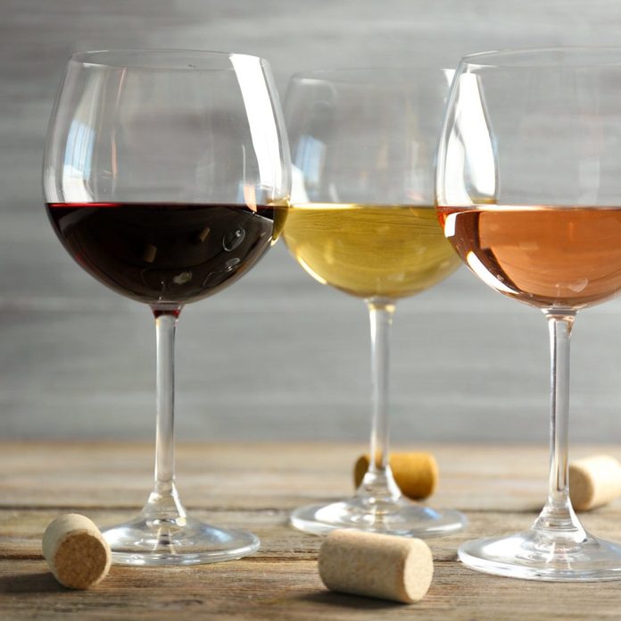 Wine glasses in a row and corks on wooden table against grey background