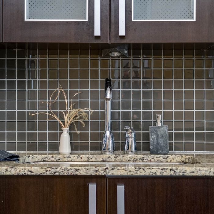 small square black tile backsplash above a kitchen counter with dark cabinets