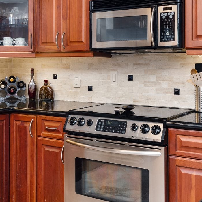 stainless steel oven and stove in a kitchen with dark cherry cabinets, a black coutnter top, and a light colored tile backsplash