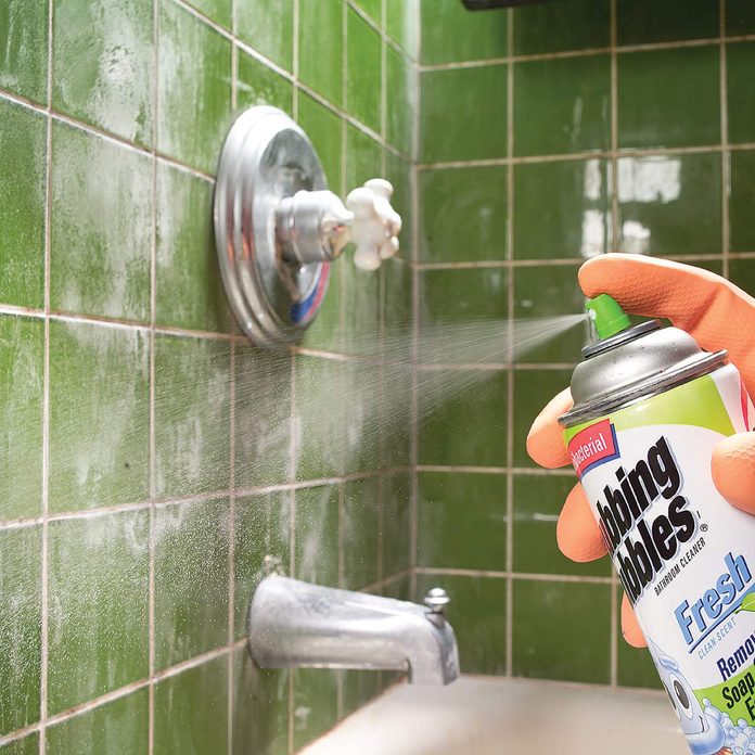 Man sprays cleaning product on shower tile