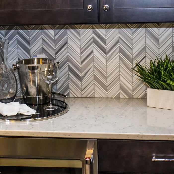 close up of white and grey chevron black splash with a light stone countertop and dark wood cabinets
