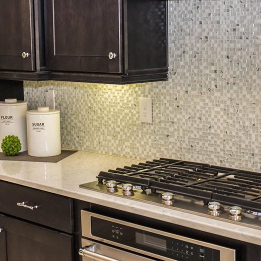 small white and grey square tile mosaic backsplash with a light countertop and black cabinets