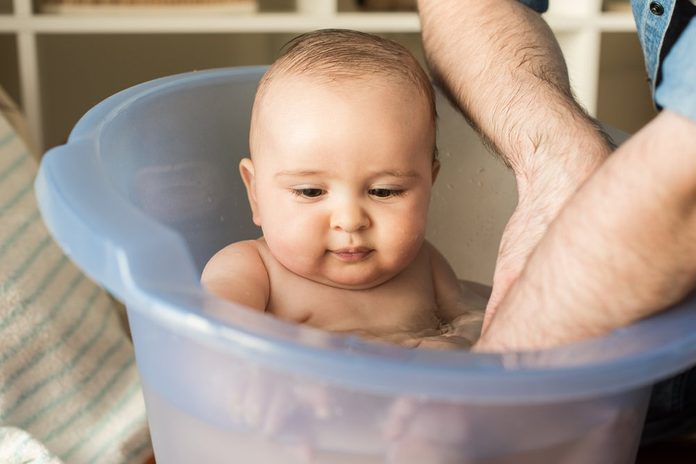 Modern father bathing his little baby with a tummy tub