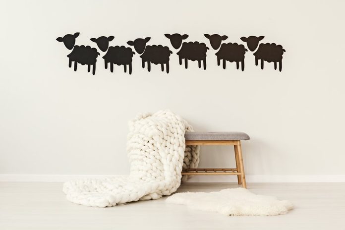 Big, handmade, woolen blanket thrown on a grey bench standing under decorative paper sheep on the wall in simple interior