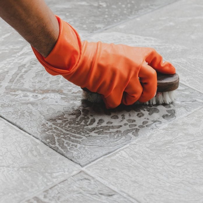 Hand of man wearing orange rubber gloves is used to convert scrub cleaning on the tile floor.; Shutterstock ID 1150384415; Job (TFH, TOH, RD, BNB, CWM, CM): TOH