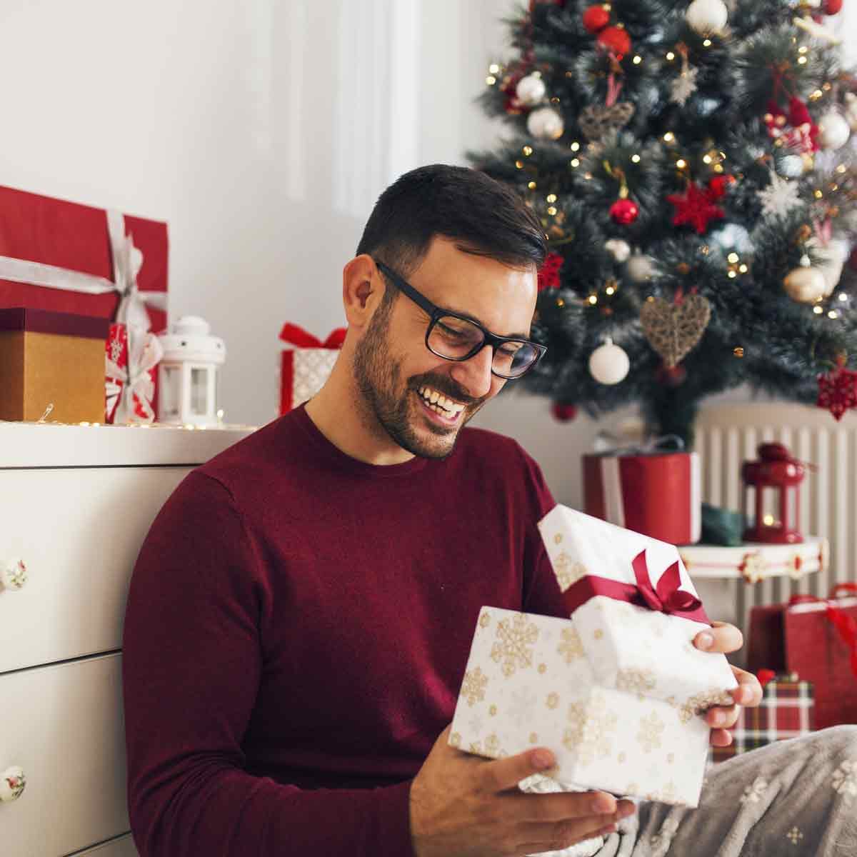 Smiling-young-man-opening-Christmas-gift-at-home