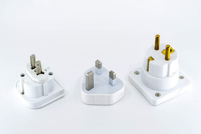 Close up view of three different travel adapter plugs for mains power isolated against a plain white background. Left to right ar the adapters for the USA, UK and Europe.