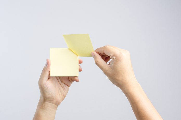 Hand holding sticky post note paper sheet on white background