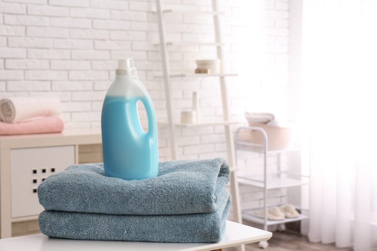 Bottle of detergent and clean towels on table indoors, space for text. Laundry day