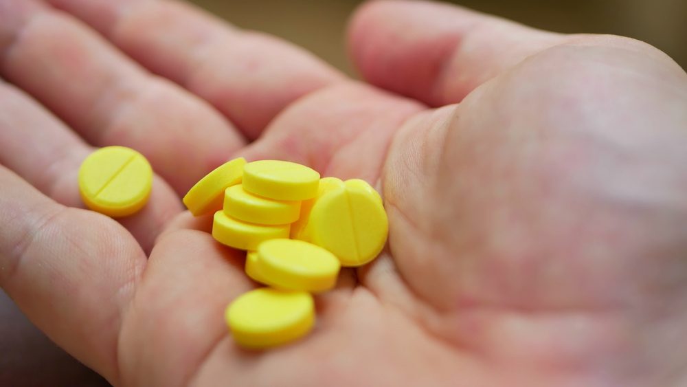 Person pouring bunch of prescription yellow opiate pills into hand