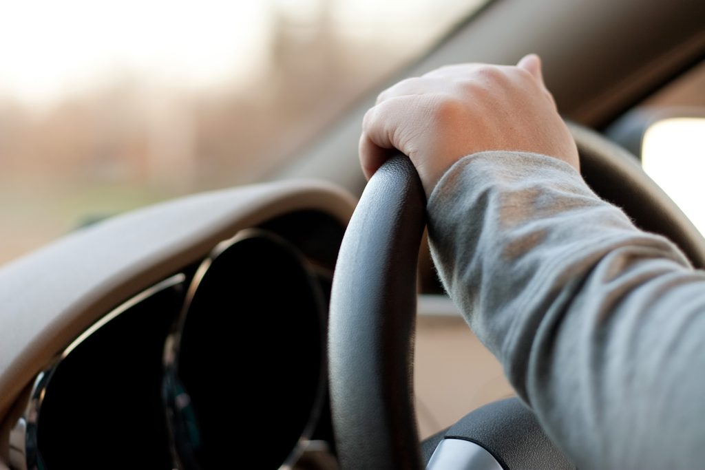 A woman holding the steering wheel of a car with one hand while driving.