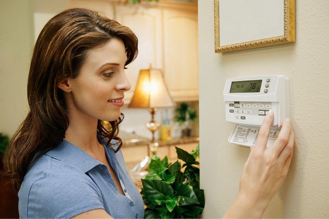 Woman Adjusting Thermostat At Home