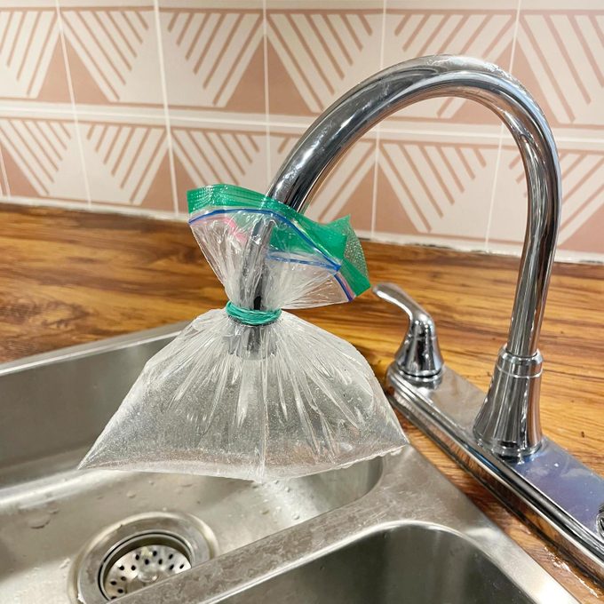 a plastic bag filled with vinegar being held onto a kitchen sink faucet with a rubber band
