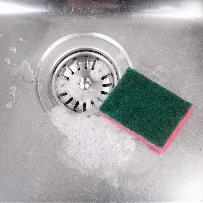 Stainless steel kitchen sink with soap suds and cleaning sponge